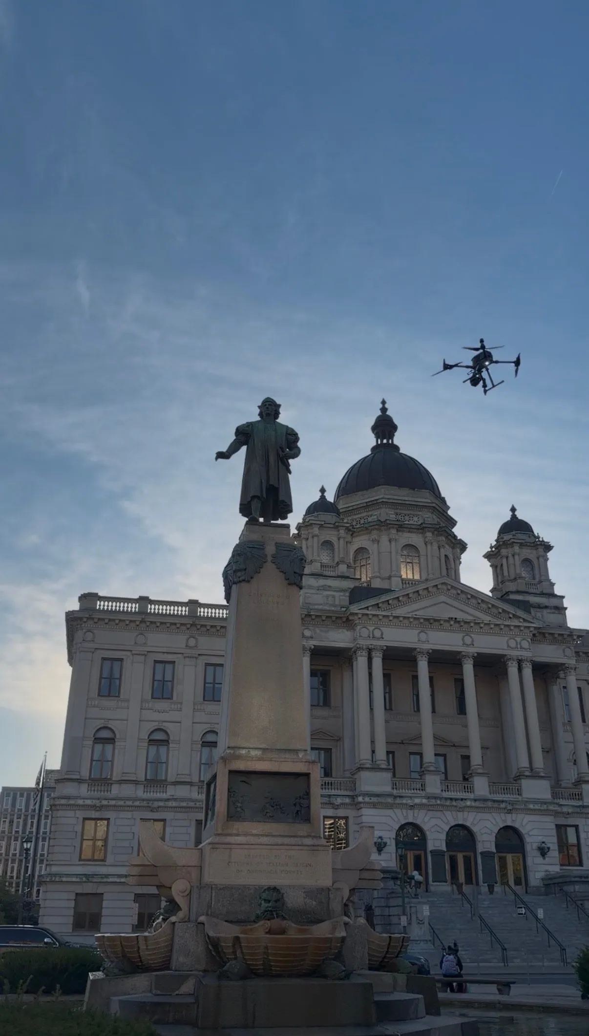 A drone flying beside the Columbus Monument, with the domed courthouse behind it