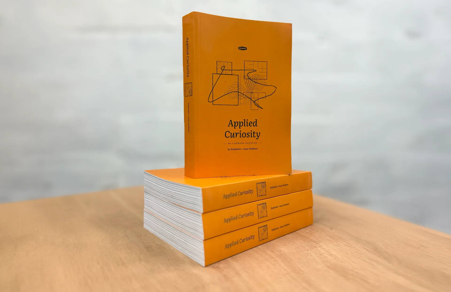 Applied Curiosity, a yellow paperback, standing upright on a stack of three copies